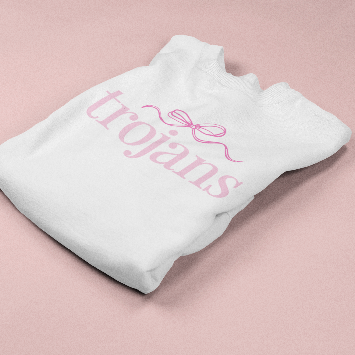 White sweatshirt with 'trojans' text and pink bow on a pink background